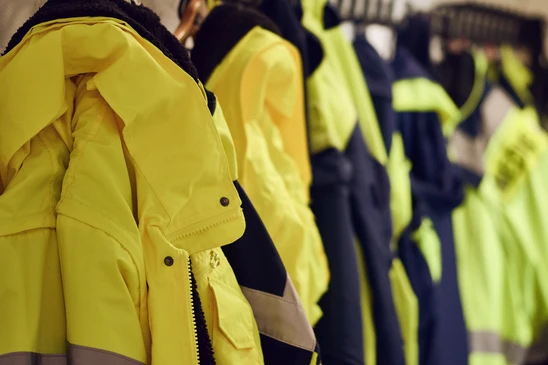Rangée de vestes de travail haute visibilité jaunes suspendues sur cintres, avec vêtements bleu marine en arrière-plan