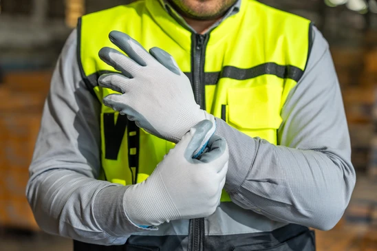 Paire de gants de travail en tricot gris posés sur fond blanc, avec liseré orange au niveau des poignets