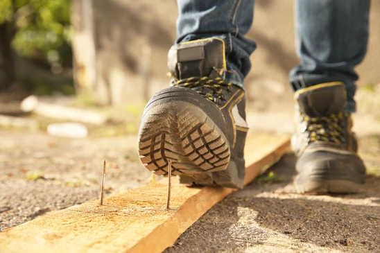 Personne assise sur des marches en béton, attachant une chaussure de sécurité noire avec lacets orange